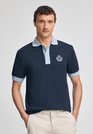 Polo blu navy con colletto e polsini azzurro chiaro; presenta un piccolo logo ricamato sul petto; maniche corte, vestibilità rilassata.