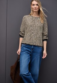 Pullover leggero con stampa leopardata, maniche lunghe e bordi neri. Abbinato a jeans blu a vestibilità rilassata e una borsa in suede marrone.