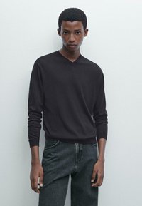 Schwarzer V-Ausschnitt-Pullover aus einem weichen, leichten Material, kombiniert mit dunklen Jeans. Der Pullover hat lange Ärmel und einen lässigen Schnitt.