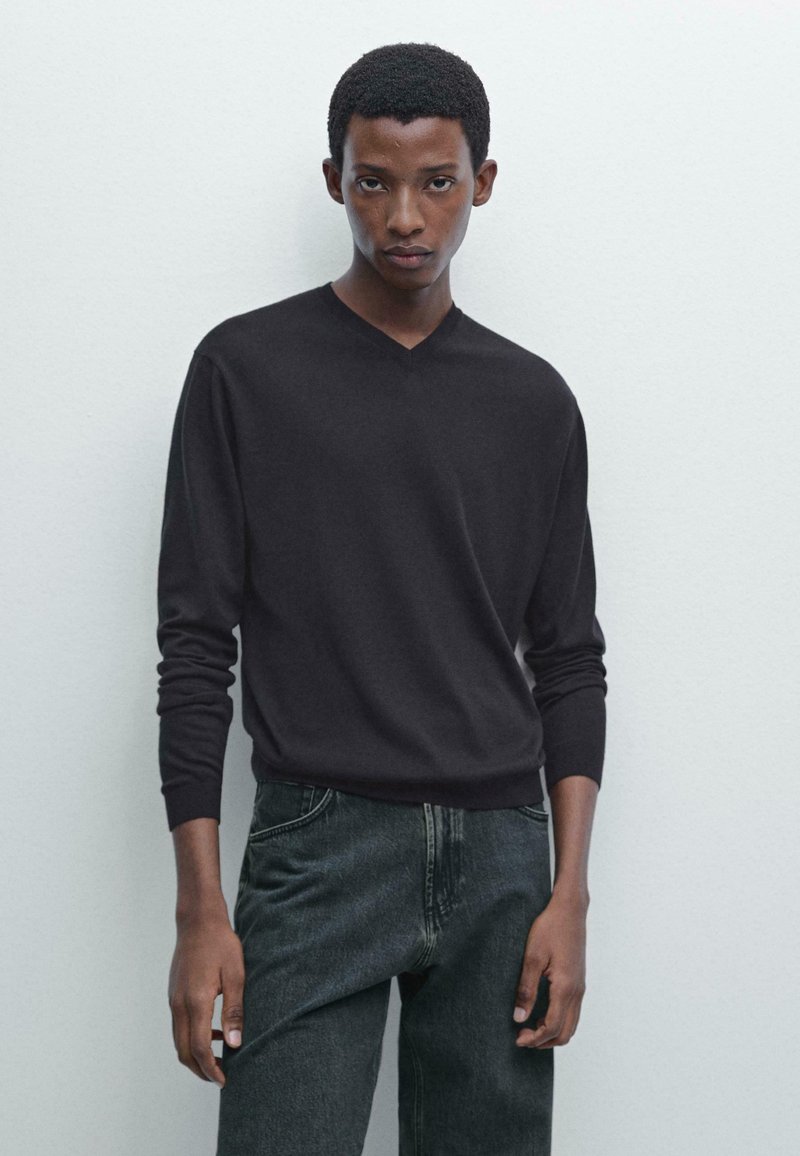 Schwarzer V-Ausschnitt-Pullover aus einem weichen, leichten Material, kombiniert mit dunklen Jeans. Der Pullover hat lange Ärmel und einen lässigen Schnitt.