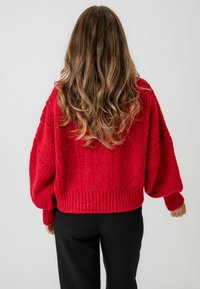 Sarkans adīts džemperis ar kubisku dizainu, ribotu apakšu un vīriņa piedurknēm. Mīksta tekstūra un brīvs piegriezums, apvienots ar melniem biksēm.