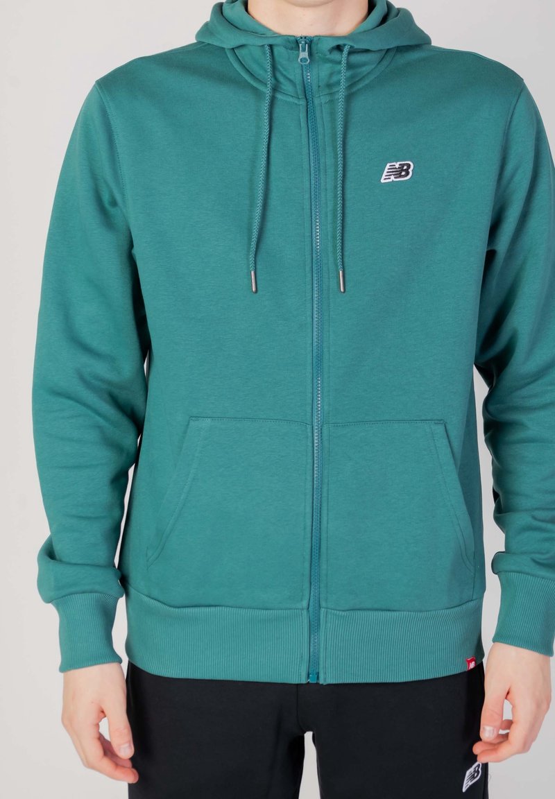 Tealfärgad zip-up hoodie med två framfickor, ribbad mudd och nederkant, justerbar dragsko på huven och en liten logotyp på vänster bröst.