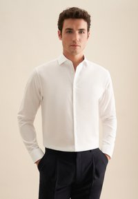 Witte langemouwen shirt met een button-down kraag, voorzien van een textuurstof en een aansluitend ontwerp, gecombineerd met donkere broek.