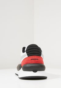 Red and gray athletic shoe with a textured suede accent, padded black heel counter, and a rounded black outsole.