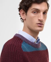 Sweter dzianinowy w kolorze burgundowym z akcentami w odcieniach zielonego i lawendowego, z prążkowaną strukturą i okrągłym dekoltem, założony na jasnoniebieską koszulę.