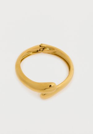 Glatt, skinnende guldfarvet armbånd med hængslet lås, der har to afrundede ender, som bøjer sig blidt mod hinanden.