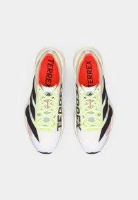 Ελαφριά αθλητικά παπούτσια σε λευκό και μαύρο, με επάνω μέρος από αεριζόμενο δίχτυ, φώσφοριζουσες κίτρινες κορδόνια και κόκκινους εσωτερικούς πάτους με το λογότυπο "TERREX".