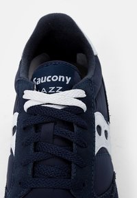 Navy blue athletic shoe featuring a suede and textile upper, white logo accents, textured laces, and padded collar for comfort.