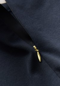 Marineblauwe stof met een gladde textuur toont een gouden ritssluiting met een afgeronde trekker, deels open, waarbij de binnenlaag zichtbaar is.