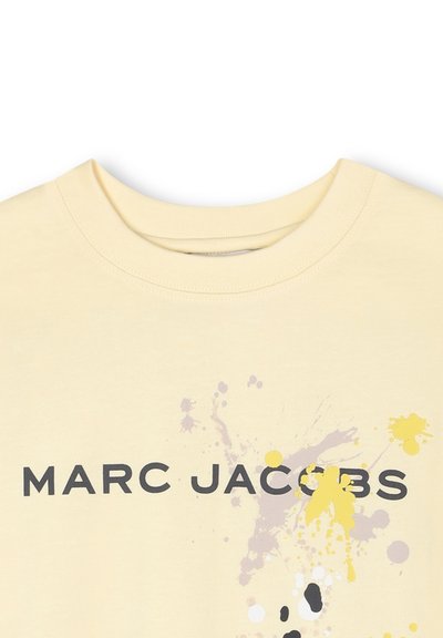 Lichtgele katoenen t-shirt met ronde hals, zwarte tekst "MARC JACOBS" en kleurrijke verfspatten in geel, grijs en zwart.