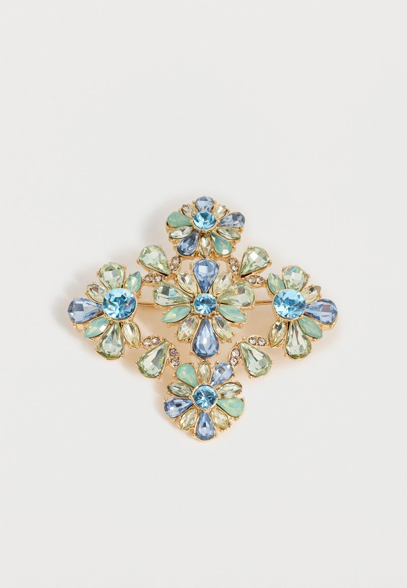 Πολυτελές χρυσό κονκάρδα με τέσσερα σχήματα λουλουδιών από μπλε, πράσινες και διαφανείς πολύγωνες πολύτιμες πέτρες, τοποθετημένες σε συμμετρικό σχέδιο.