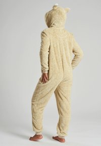 Beige fleecedon met een capuchon en berenoren. Geweven, zachte stof. Voorzien van zijzakken en boorden bij de enkels en polsen.