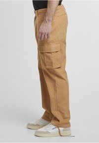 Pantaloni cargo bej din catifea cu buzunare laterale și croială dreptă, asortați cu adidași albi și bej. Material texturat vizibil.