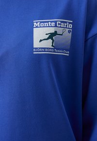 Μπλε βαμβακερό T-shirt με γραφική εκτύπωση που περιλαμβάνει το κείμενο "Monte Carlo" και μια περίγραμμα ενός τενίστα, μαζί με το "BJÖRN BORG Tennis Club."