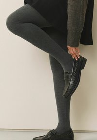 Sivé pletené legíny v kombinácii s čiernymi mokasínami, ktoré majú prešité detaily a hladkú textúru, zobrazené na neutrálnom pozadí.