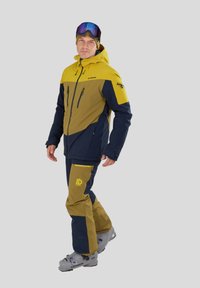 Completo da sci giallo e blu navy, con una giacca dotata di molteplici tasche con zip e pantaloni coordinati con dettagli del logo e sezioni a contrasto.
