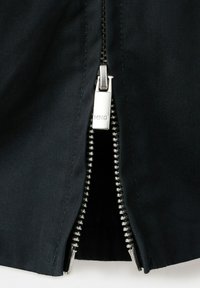 Približnji posnetek delno odprtega črnega zadrge s srebrnimi kovinskimi zobmi in potegom na črnem blagu.