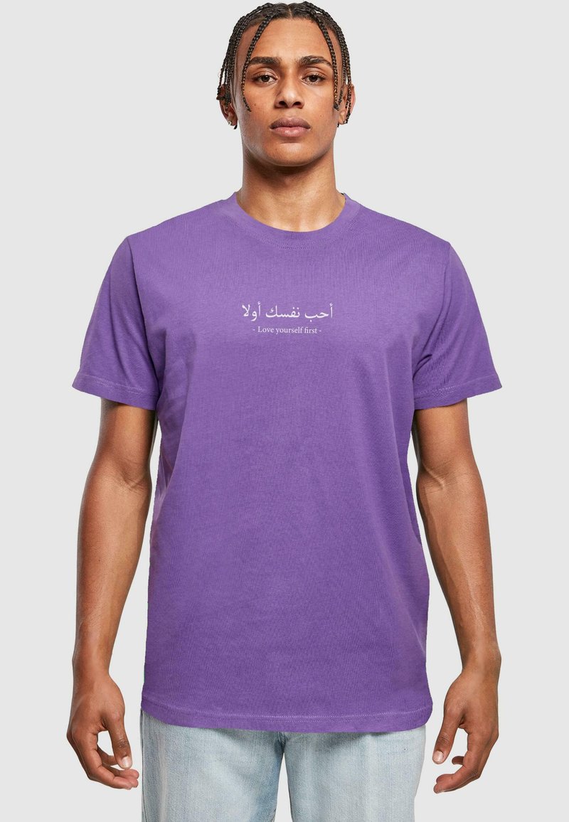Camiseta de algodón morada con mangas cortas y escote redondo. El texto en árabe e inglés dice: "Ámate a ti mismo primero."