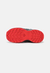 Suela de zapatilla deportiva negra y roja con un dibujo de goma texturizada para mayor agarre, con surcos prominentes y un patrón triangular.