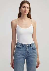 Witte camisole met dunne bandjes, gecombineerd met hoge lichtblauwe jeans, met een klassieke denimmerk en een voorknopsluiting.