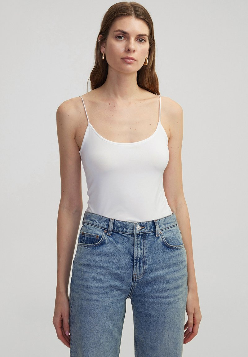 Witte camisole met dunne bandjes, gecombineerd met hoge lichtblauwe jeans, met een klassieke denimmerk en een voorknopsluiting.