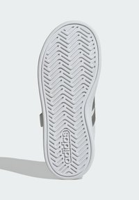 Bílá gumová podrážka boty se vzorem běhounu ve tvaru zubatého klínu a vyraženým logem „adidas“. Má hladké okraje a strukturovaný design.