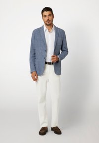 Šviesiai mėlynas lino ir vilnos mišinuko švarkas su įpjovomis ant apykaklės, vienu krūtiniu kišeniu, derinamas su balta marškiniu, kreminėmis kelnėmis ir rudais loaferiais.