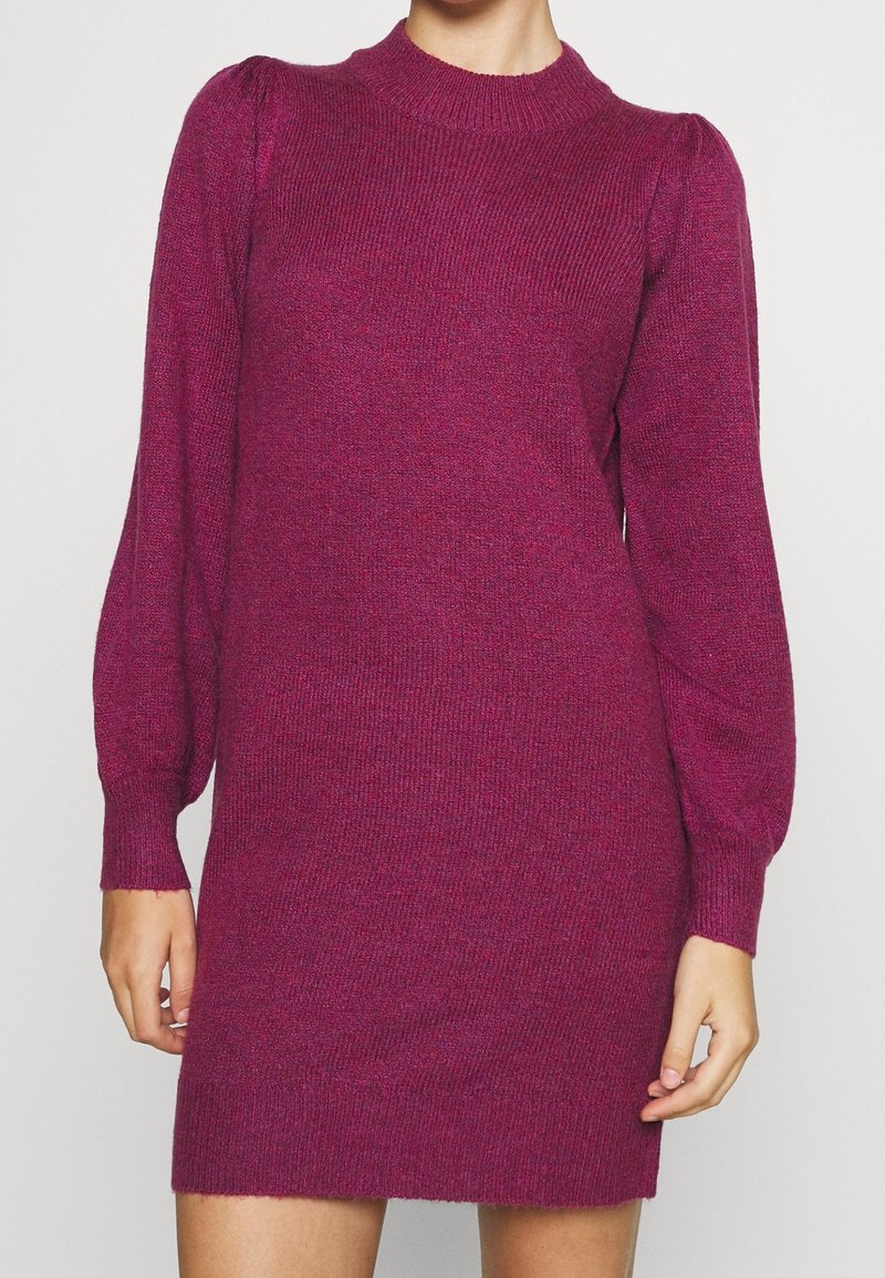 Robe en tricot fuchsia avec une texture côtelée, des manches longues bouffantes et un col rond, présentant une silhouette légèrement cintrée et un ourlet à mi-cuisse.