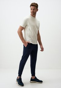 Lichtbeige t-shirt met korte mouwen, gecombineerd met donkerblauwe aansluitende broek en donkere sneakers. Soepele textuur, eenvoudig ontwerp en geen zichtbare patronen.