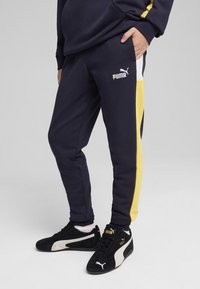 Granatowe dresy z żółtym paskiem po boku. Posiadają białe logo Puma na udzie oraz ściągacze na nogawkach. W komplecie z czarnymi i białymi sneakersami.