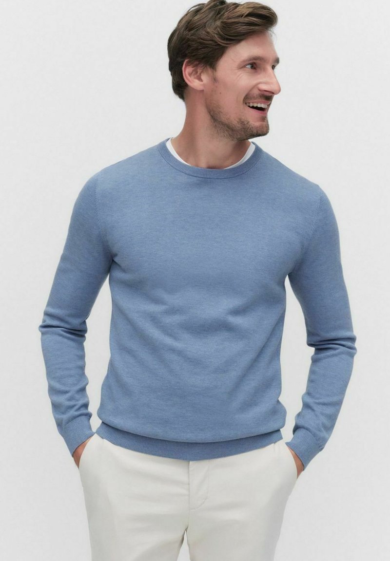 Ljusblå stickad tröja med rund halsringning och ribbade ärmslut, tillsammans med vita byxor med en enkel och slät textur.