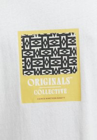 Balta marškinėliai su geltona stačiakampio formos grafika, juodu geometriniu raštu ir balta užrašu "ORIGINALS COLLECTIVE" apačioje.