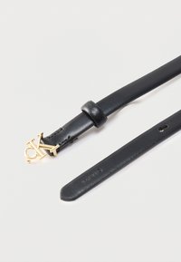 Μαύρη δερμάτινη ζώνη με χρυσή αγκράφα 'CK' και θηλιά ζώνης, με ανάγλυφο λογότυπο Calvin Klein κοντά στο μυτερό άκρο, σε λευκό φόντο.