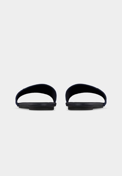 Ζευγάρι μαύρων σανδαλιών χωρίς κορδόνια με φαρδιές λουρίδες και επίπεδες σόλες, εμφανιζόμενα από μπροστά σε λευκό φόντο.