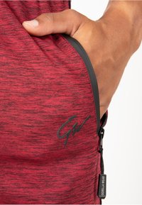Rood gemêleerd stof met een gestructureerde afwerking. Beschikt over een zwart ritsvak, een gemarkeerd logo en contrasterende stiksels voor extra duurzaamheid.