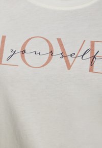 Weißes Baumwoll-T-Shirt mit dem Aufdruck "LOVE yourself" in korallen- und marineblauer Schrift. Das Design hat eine weiche Textur und einen schlichten runden Ausschnitt.