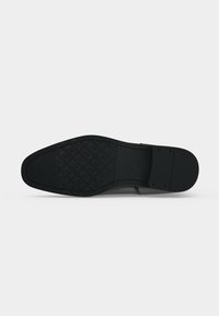 Semelle d'une chaussure habillée noire avec une semelle en caoutchouc à motif à l'avant et un talon lisse, présentée sur un fond clair uni.