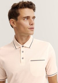 Helle rosa Poloshirt mit klassischem Kragen, drei Knopfleiste und kontrastierenden marineblauen Akzenten am Kragen und an der Tasche. Material aus Baumwollmischung.