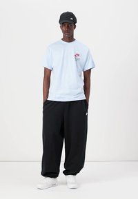 Gaiši zils kokvilnas T krekls ar sarkano Nike logotipu, saskaņots ar brīviem melniem sporta biksēm un baltām apaviem, papildināts ar melnu cepuri.