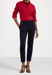 Röd linneknappad skjorta med upprullade ärmar, kombinerad med marinblå skräddarsydda byxor och svarta remsandaler. Minimalistisk guldaccessoar.