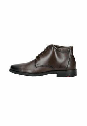 Botín de cuero marrón con un acabado suave, punta redonda, seis ojetes para atar los cordones y un bajo tacón de goma negra.