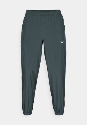 Nike tepláky v tmavovzelenom odtieni, s elastickým pásom, zúženým strihom nohavíc a jemným reflexným logom na boku.