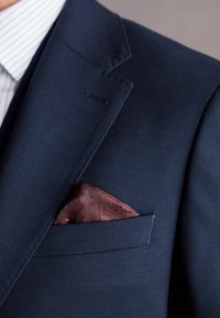 Marynarski blezer w granatowym kolorze, wykonany z teksturowanej tkaniny, z poszetką w kolorze burgundowym o subtelnym wzorze, umieszczoną w lewej kieszeni.