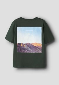 Ciemnozielona bawełniana koszulka z graficznym motywem gór o zachodzie słońca na przodzie, z niebieskim niebem, otoczona białym geometrycznym konturem.