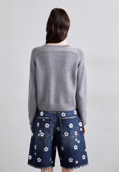 Suéter de punto gris con cuello redondo, combinado con shorts de mezclilla oscura que presentan bordados florales blancos y bolsillos frontales.