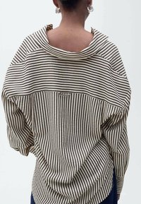 Chemise ample à rayures présentant des rayures noires et crème horizontales et verticales, avec un large décolleté et des coutures d'épaule tombantes. Texture lisse.