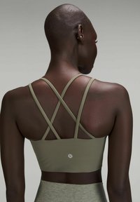 Sujetador deportivo de color verde oliva con tirantes cruzados, que cuenta con una tela suave y elástica y un pequeño logo en la parte posterior.