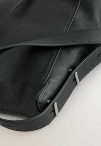 Borsa a tracolla in pelle nera con finitura testurizzata, dotata di una tracolla piatta e dettagli in argento. Design semplice e minimalista senza hardware visibile.