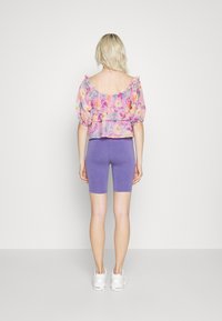 Haut court à fleurs avec manches bouffantes, en nuances de rose et jaune, assorti à un short de cycliste violet. Des baskets blanches complètent la tenue.