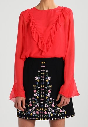 Czerwona bluzka z długim rękawem i falbaną w kształcie litery V z przodu, zestawiona z czarną spódnicą z kolorowym kwiatowym haftem na środku.